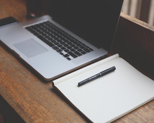 Asian man stretching arms while sitting at a home office desk looking away from laptop